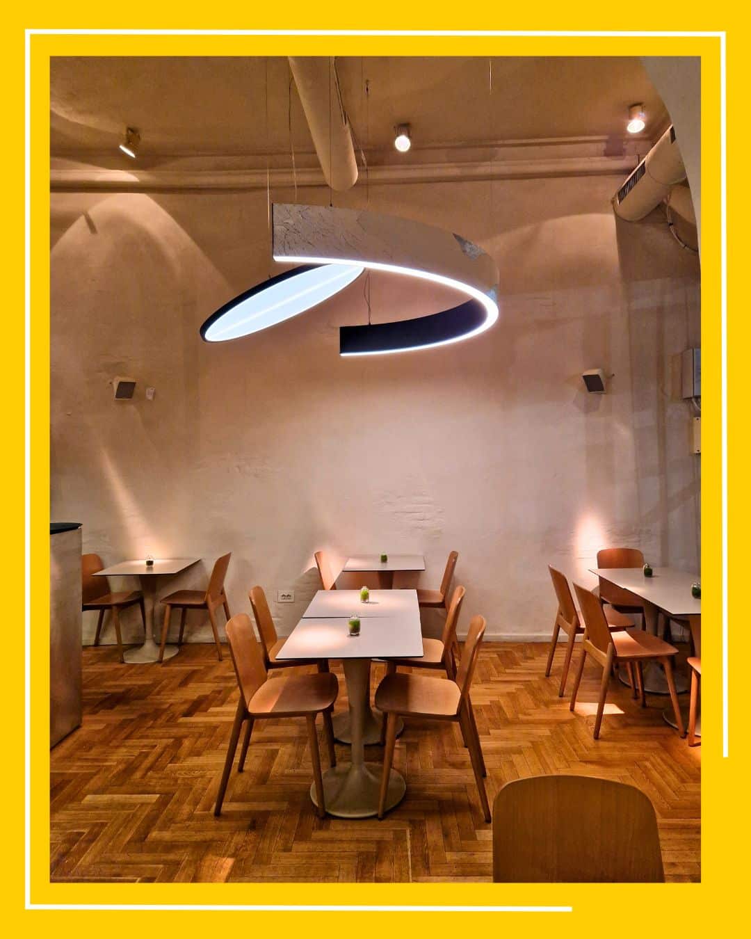 imagine din interiorul restaurantului MOM București, cu scaune din lemn si mese bej, si un corp de iluminat modern deasupra