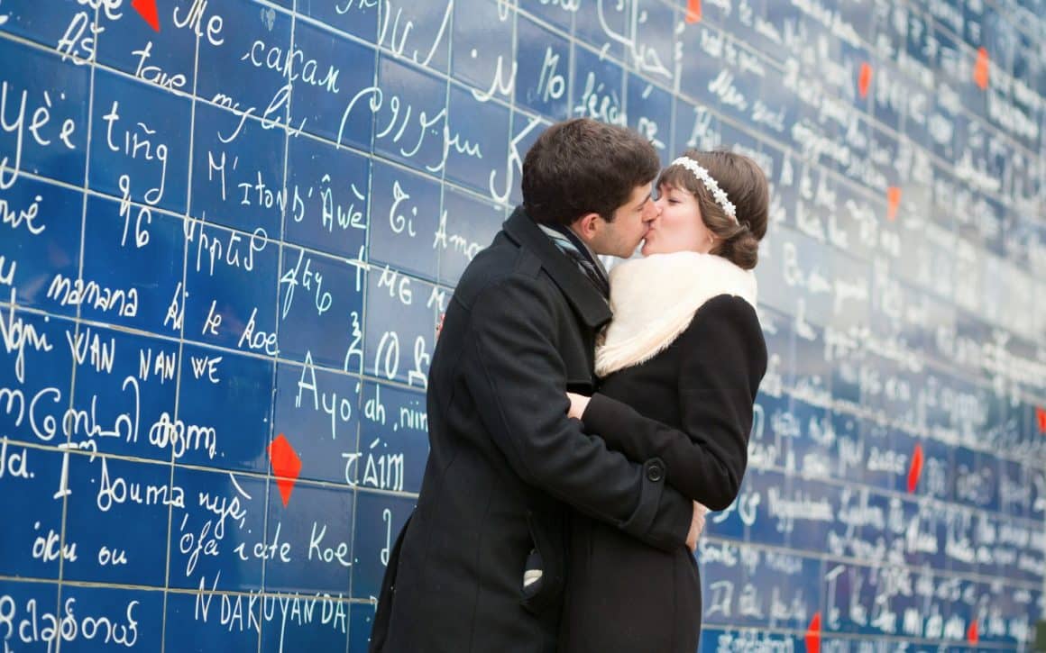 un cuplu se saruta in fata Wall of Love din Paris