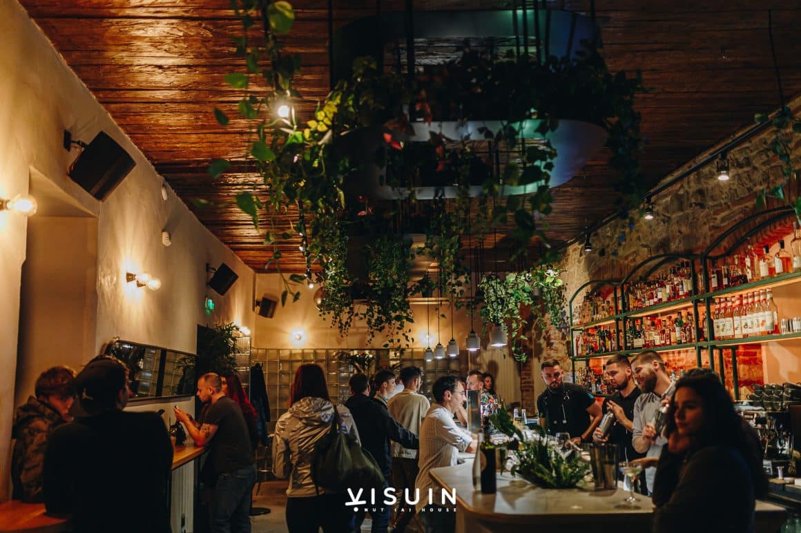 Mai multi oameni isi petrec seara in barul Visuin din Cluj, decorat cu plante si un bra elegant