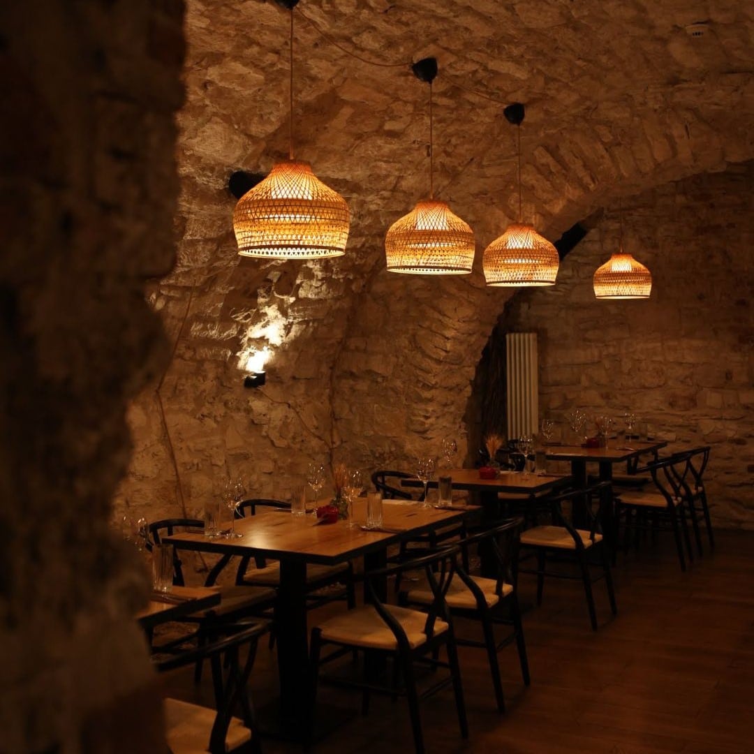 mese amplasate intr-o crama din cadrul restuantului Nativ, fotografiate in lumina difuza, cu abajururi aprinse deasupra. restaurante Cluj