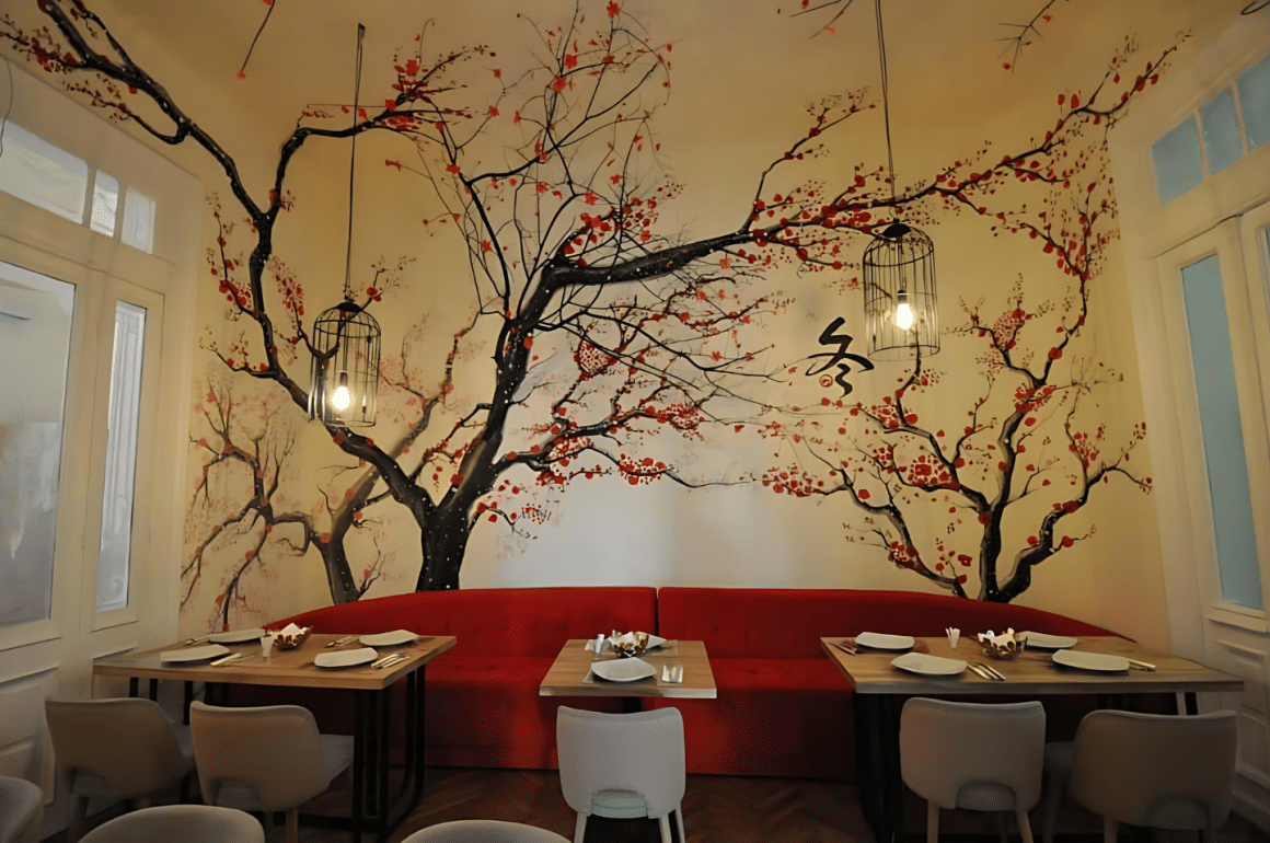 Incapere din restaurant Peng You, cu un perete desenat cu ciresi infloriti, canapea mare rosie, din catifea, si mese pentru clienti. Top restaurante chinezești București