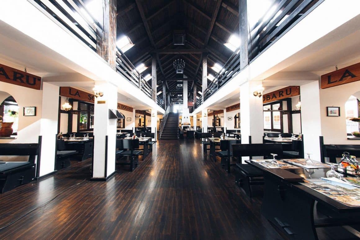 Imagine de ansamblu din restaurant Taverna Sarbului, cu mobilier din lemn negru si pereti albi, si scari care conduc la etajul superior. Restaurante etnice cu specific deosebit