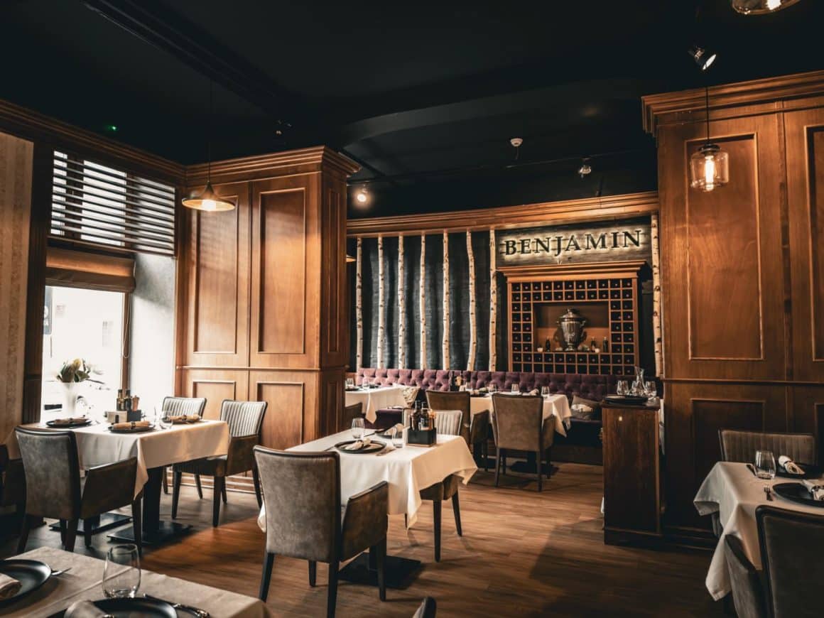 restaurant Benjamin Steakhouse, amenajat elegant, cu mese in dreptul ferestrelor si firma luminoasa in fundal, pe perete. Cele mai bune restaurante Sibiu