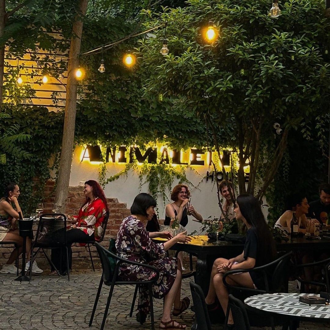 mai multi oameni iau masa pe terasa Animaletto House din București, seara, iluminata cu beculete