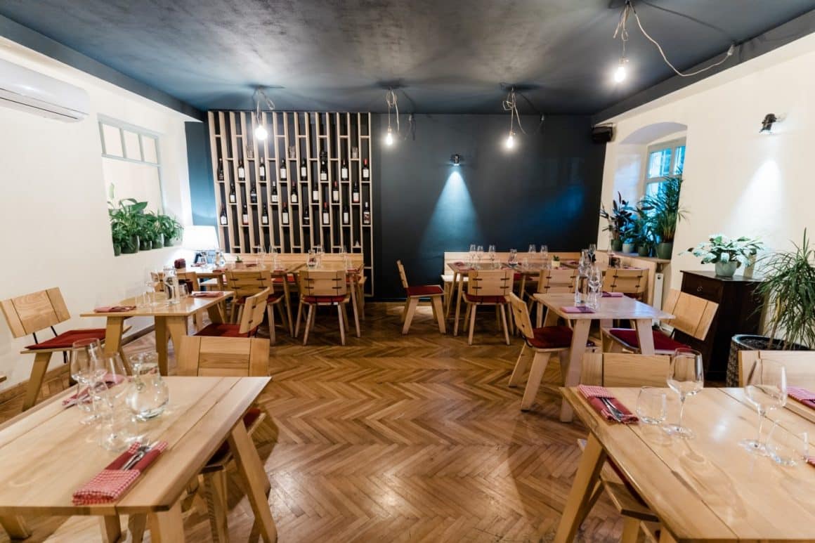 Imagine din interiorul restaurantului la Hochmeister, unul dintre cele mai bune restaurante din Sibiu. Mobilier din lemn si in fundal un perete acoperit cu rafturi de sticle de vin