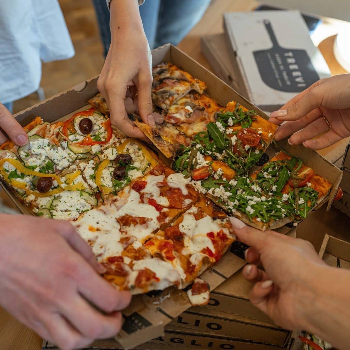 close up cu o cutie de pizza, cu 4 bucato cu toppinguri diferite, din care iau mai multi prieteni sa manance. 
