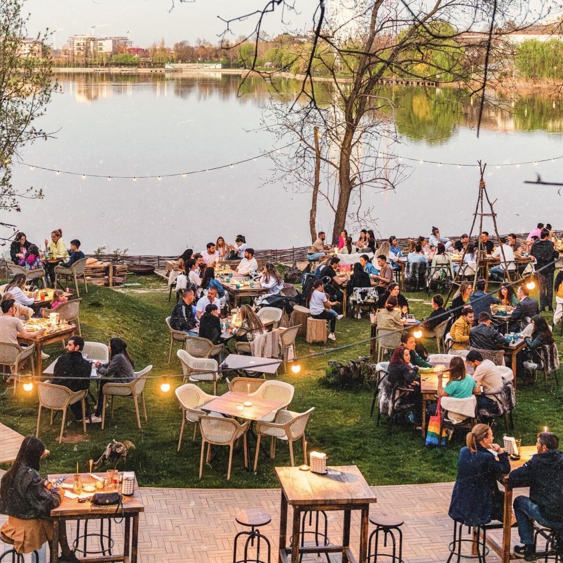 Terase București: terasa mare de la Indigen, asezata pe maulul Lacului Tei, cu multi oameni asezati la mese, pe iarba