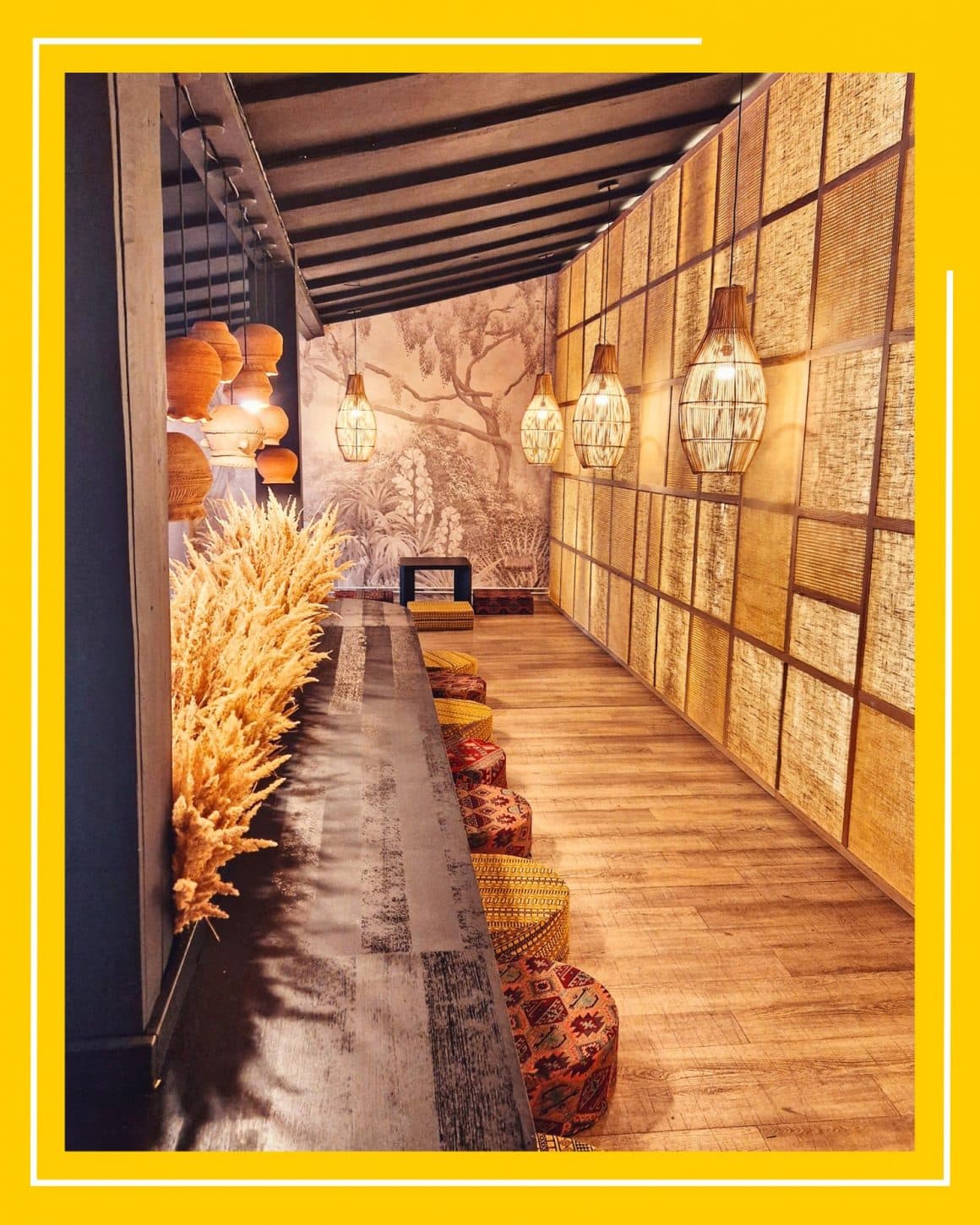 Interiorul decorat in stil asiatic, elegant, de la restaurant Momo, cu o masa joasa si tabureti pe car ese sta pe podea, multe paie decorative, candelabre din bambus si un perete cu panouri luminate
