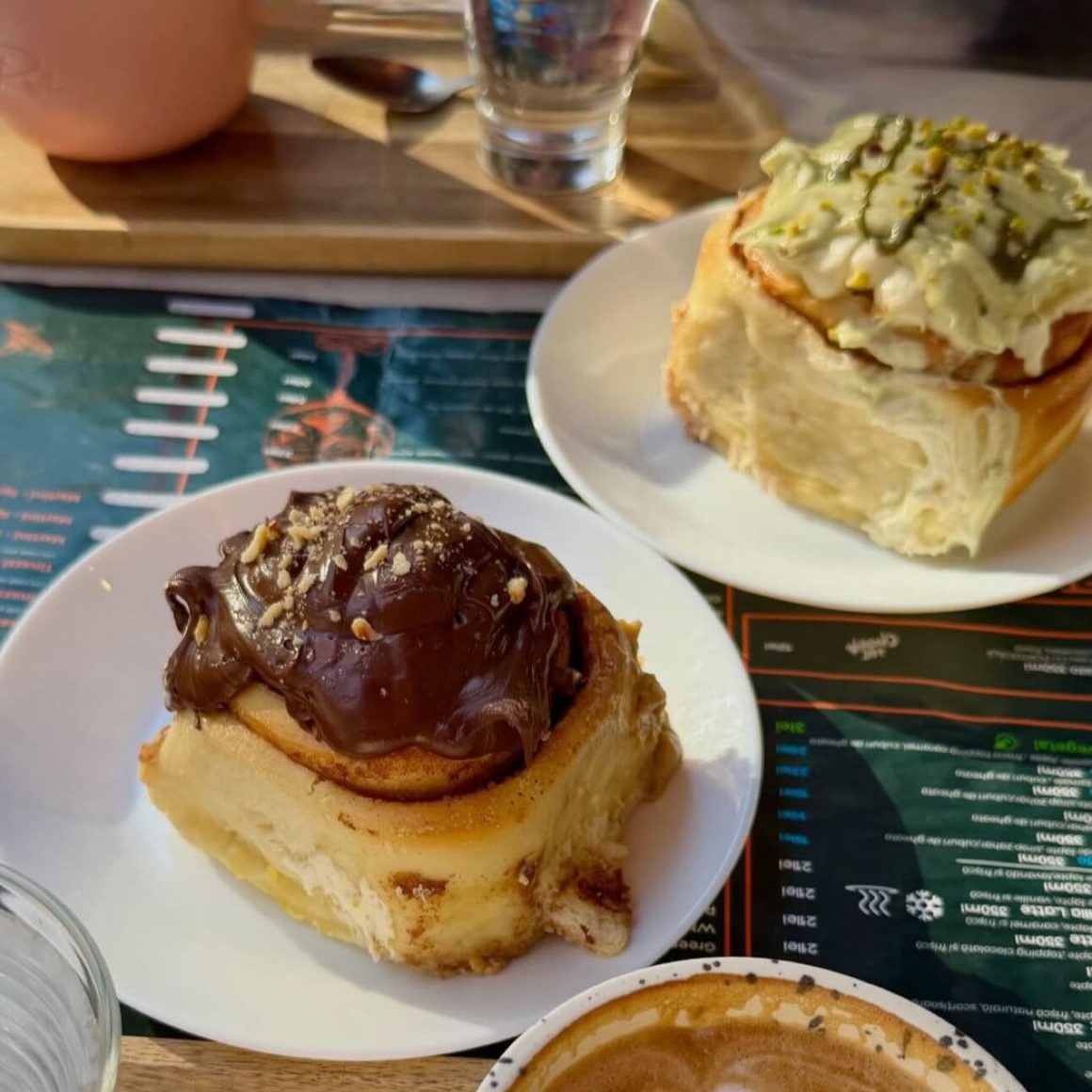 Cinnamon rolls pufoase cu topping de ciocolată și fistic, servite la La Rosta, alături de o cafea.