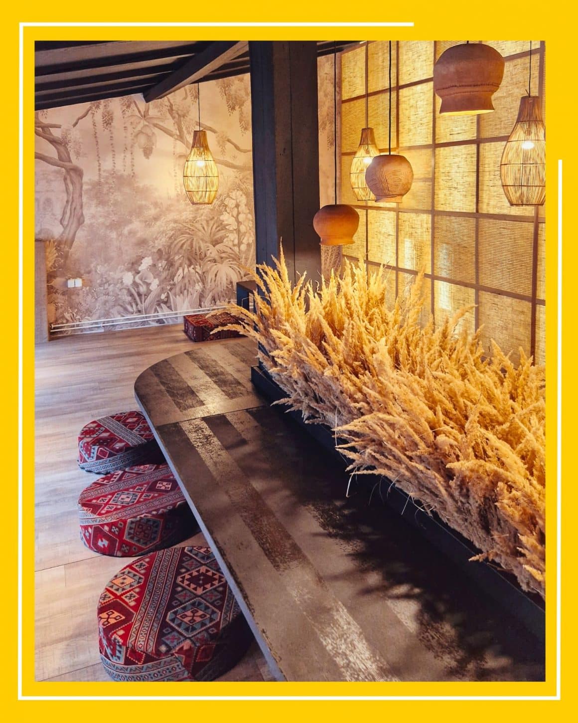 Interiorul decorat in stil asiatic, elegant, de la restaurant Momo, cu o masa joasa si tabureti pe car ese sta pe podea, multe paie decorative, candelabre din bambus si un perete cu panouri luminate