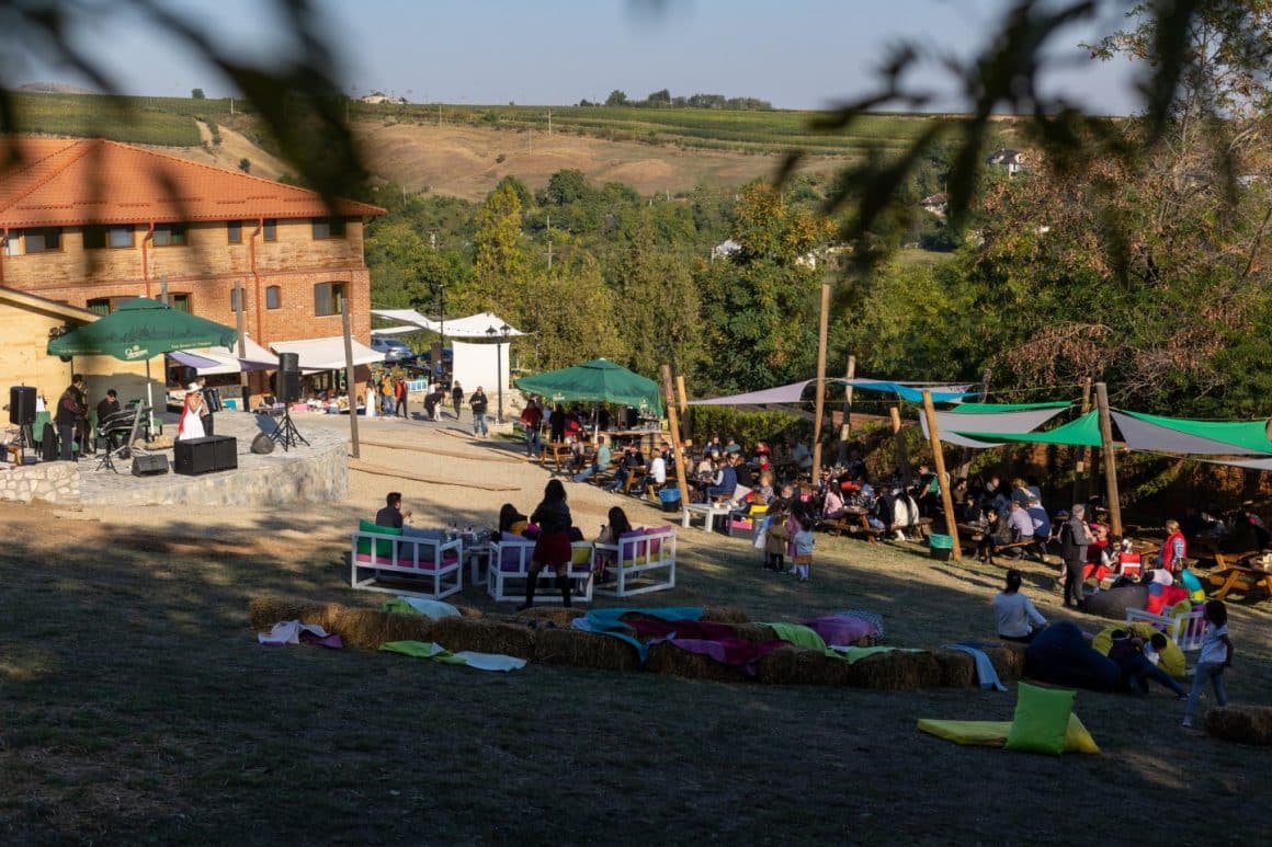 mai multi oameni iau masa pe terasa de la Crama Casa de piatră, in timp ce altii se relaxeaza pe bancute si poufi, pe iarba. restaurante langa Bucuresti