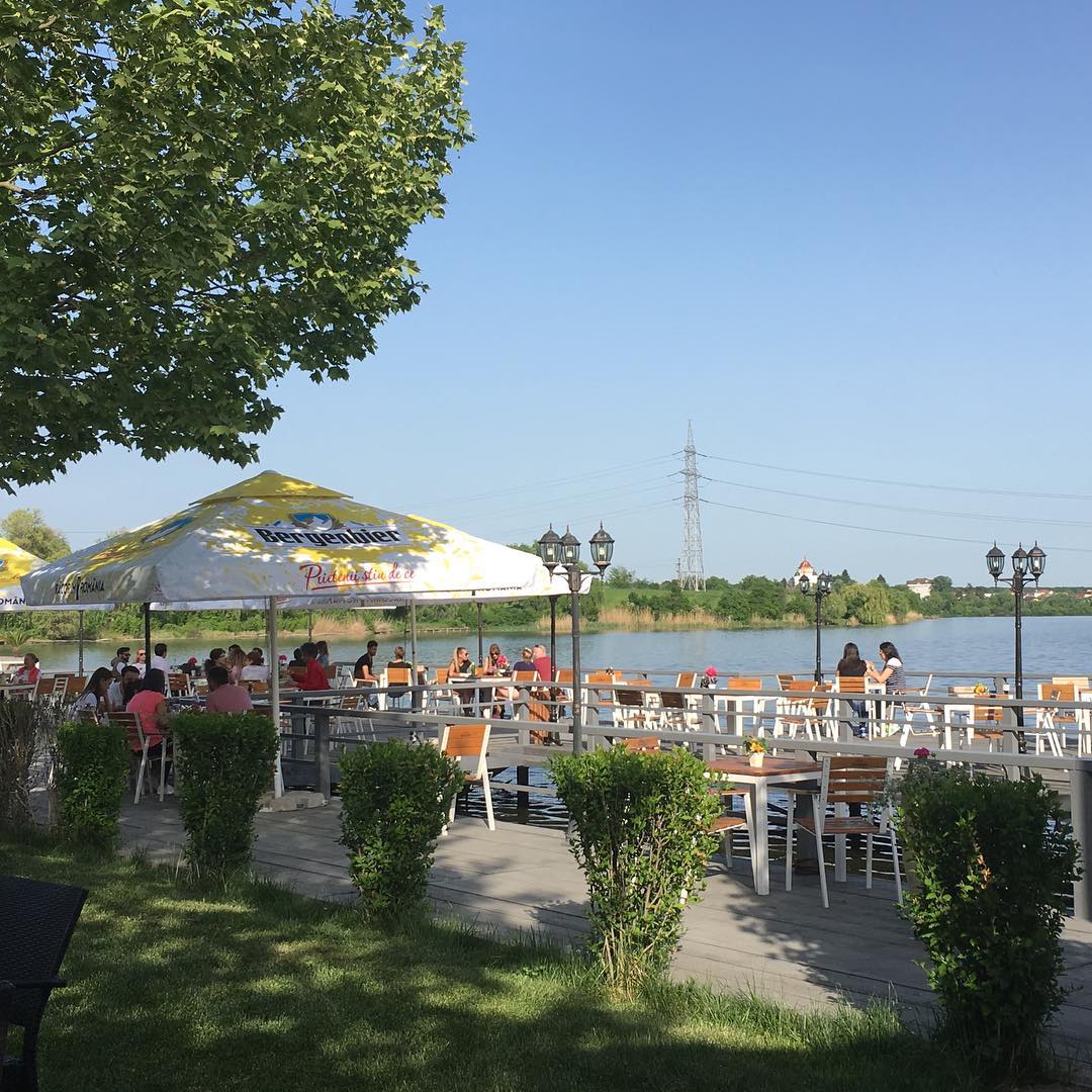 mai multi oameni iau masa la restaurant Cernica, pe ponton pe malul lacului. Restaurante lângă București