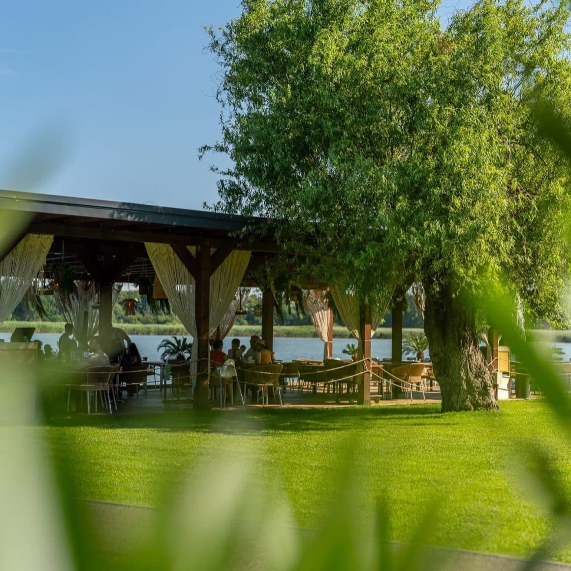 mai multi oameni iau masa pe terasa Garuda lakeside dining, din cadrul Phoenix Cernica. Fotografie in plan indepartat. restaurante lângă București