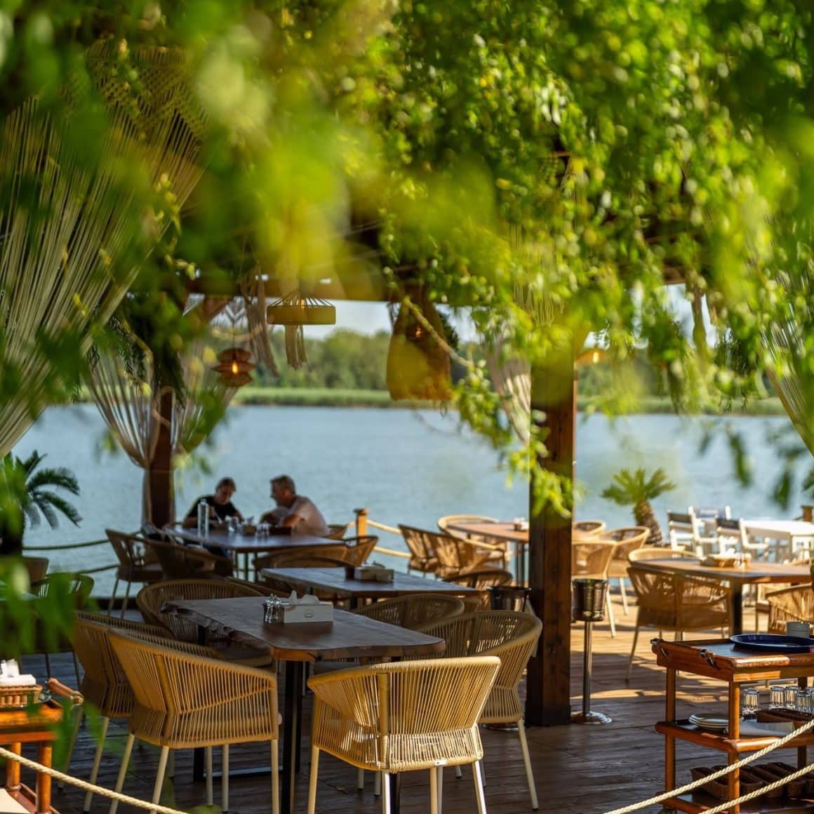 mai multi oameni iau masa pe terasa Garuda lakeside dining, din cadrul Phoenix Cernica. Fotografie in plan indepartat. restaurante lângă București