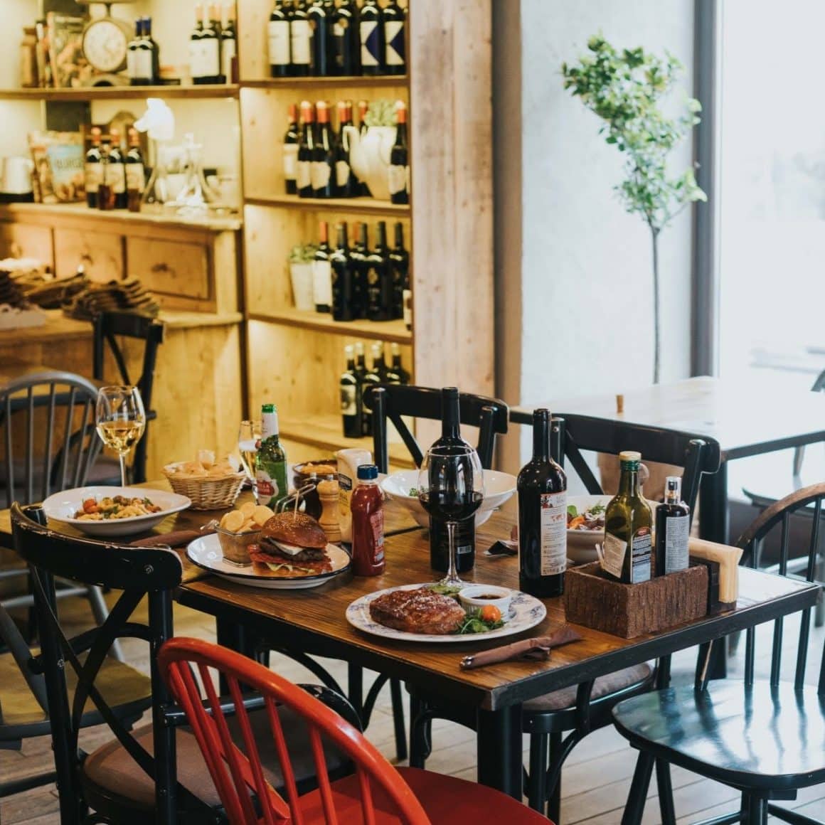 Masa plina cu farfurii cu mancare, steak si burgeri si sticle de vin, la Muura Steakhouse. Restaurante din Cluj