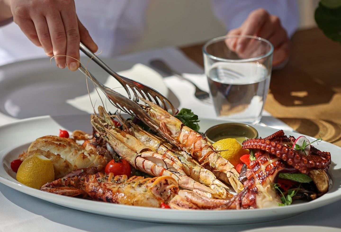 close up cu un platou mare cu fructe de mare din care mananca cineva, cu creveti, caracatita, calamar etc. Restaurante cu fructe de mare București