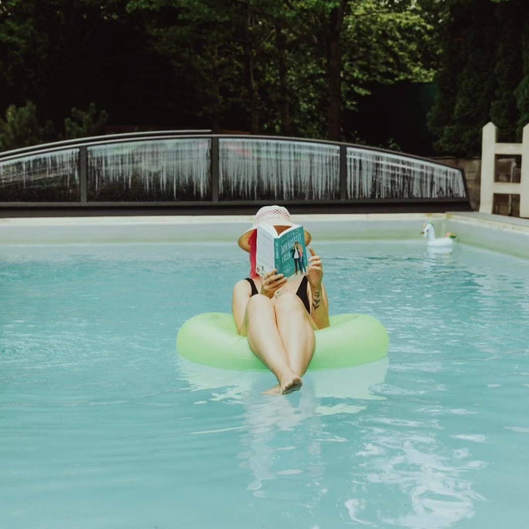 o femeie sta in colac, in piscina, cu o carte in mana