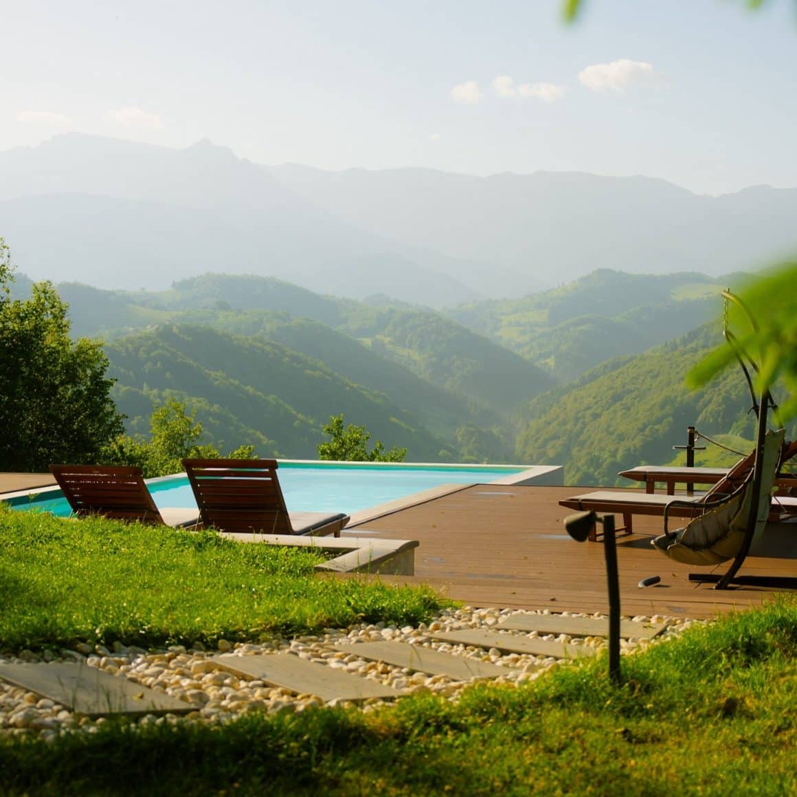 piscina exterioara si 2 sezlonguri pe margine, iar in fundal se vad muntii.