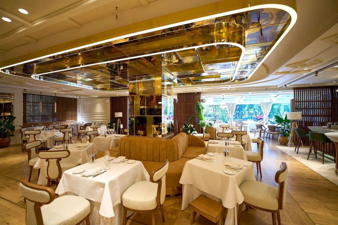 Interior Akos Restaurant, amenajat elegant, cu mese albe și detalii aurii, aproape de terasele Herăstrău.