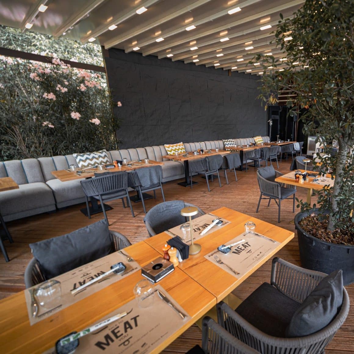 Terasă acoperită la Argentine Steak & Sushi Herăstrău, amenajată elegant cu bănci lungi, mese din lemn și plante naturale. Terase Herăstrău