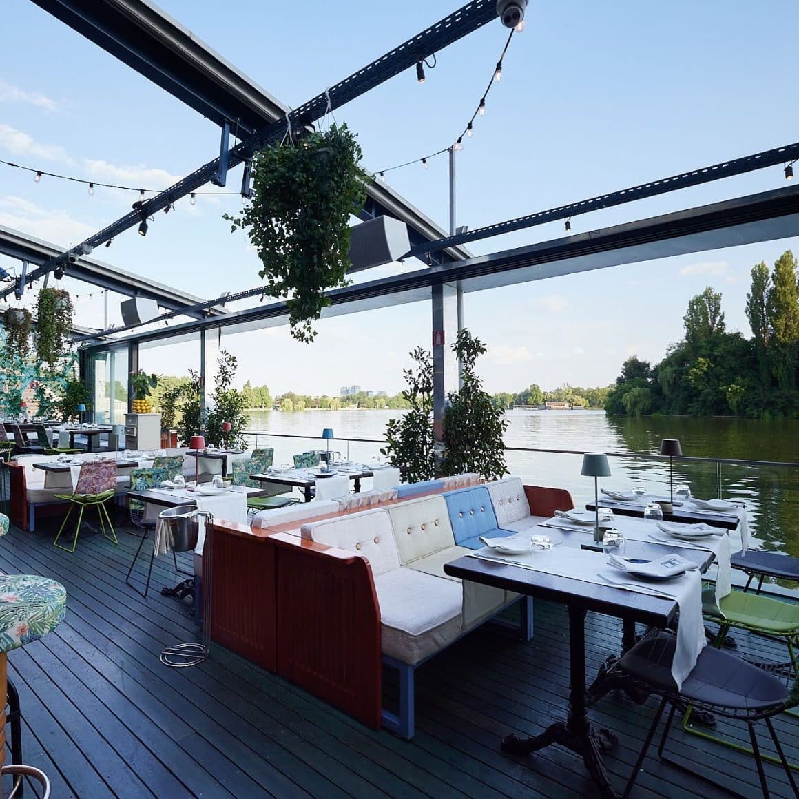 Terasa Fratelli pe malul lacului Herăstrău, cu canapele colorate, mese pregătite pentru cină și priveliște panoramică.