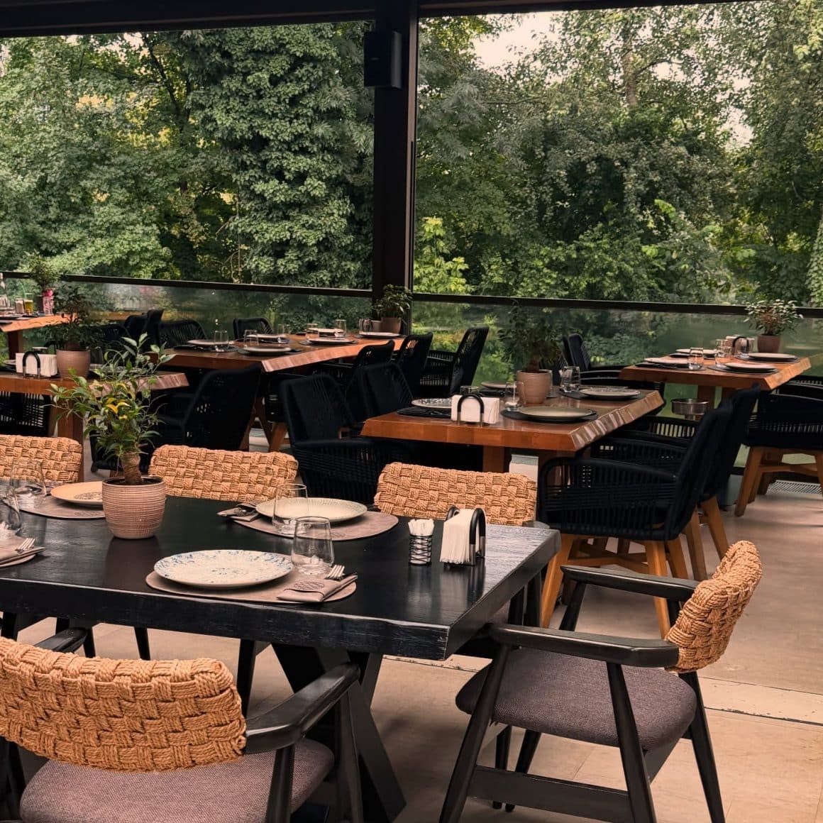 Terasă Zaitoone cu vedere spre copaci, design modern și mese pregătite pentru cină, în zona Herăstrău.