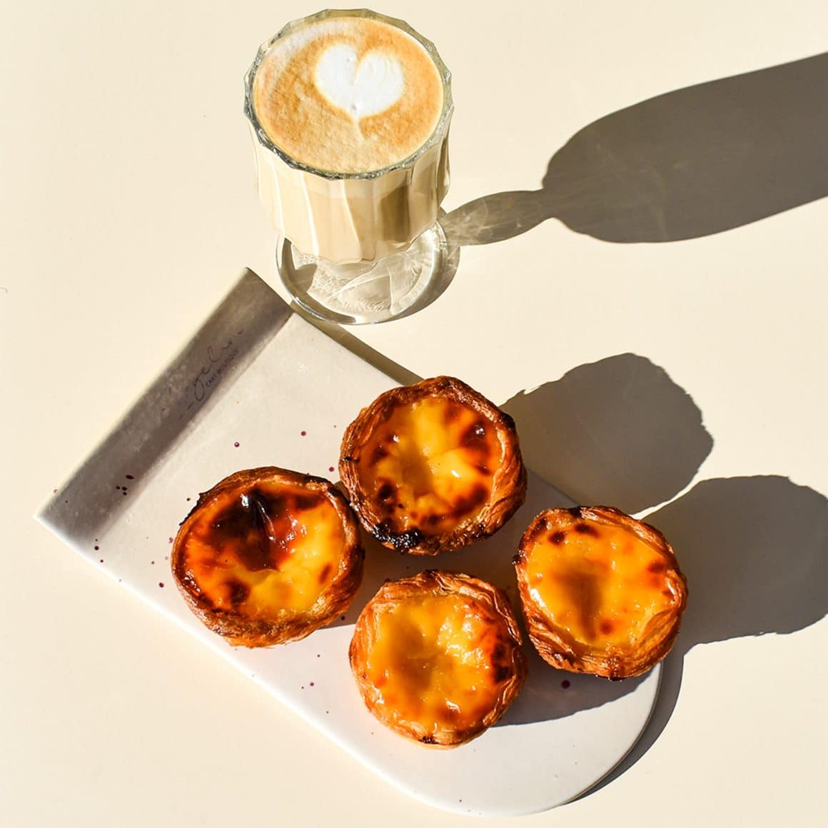 Farfurie cu pasteis de nata langa un pahar de caffe latte. De la Angeline Cake Boutique