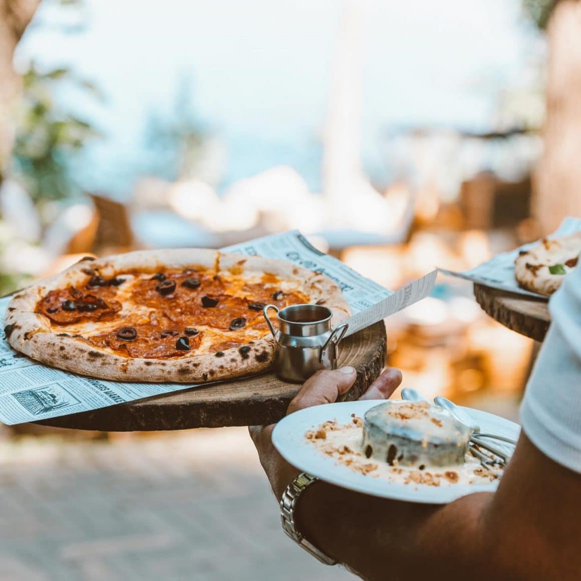 close up cu un ospatar care serveste o farfurie cu pizza si una cu desert