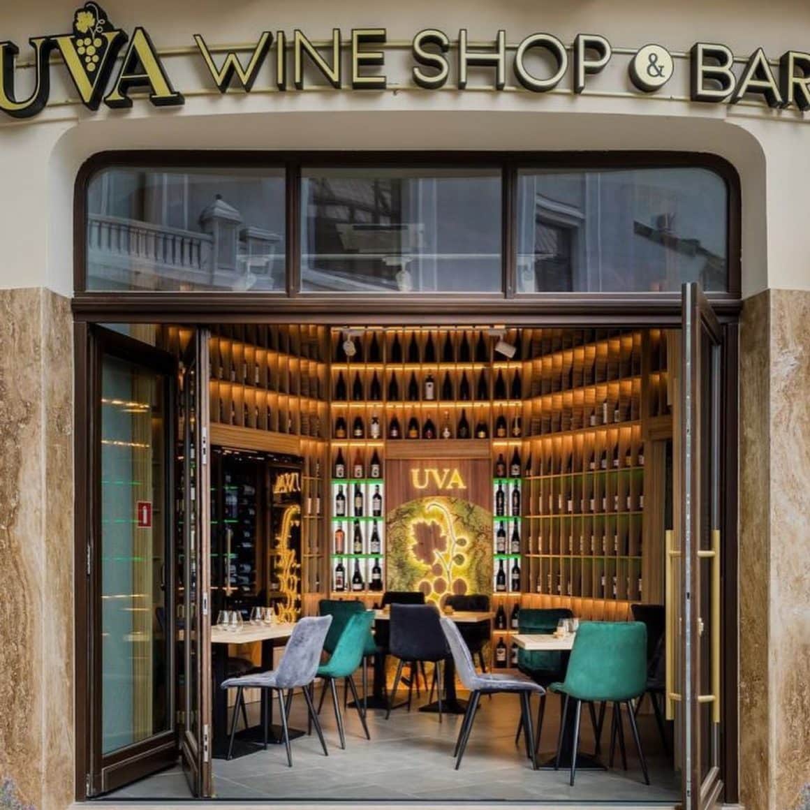 interiorul barului UVA Wine shop & Bar fotografiat din dreptul unei ferestre mari, cu mese din lemn si peretii acoperiti cu rafturi pline de sticle d evin. wine bars București