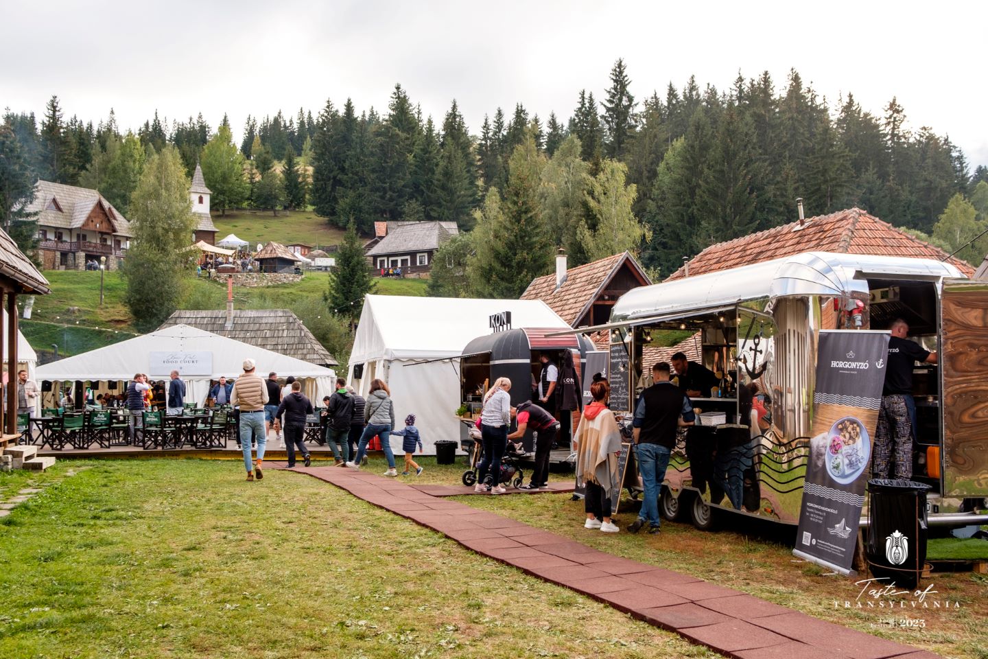 Târguri gastroniomice de toamnă: Taste of Transylvania. Casute cu produse de la mestesugari, pe o pajiste la poalele unui deal cu casute traditionale romanesti.