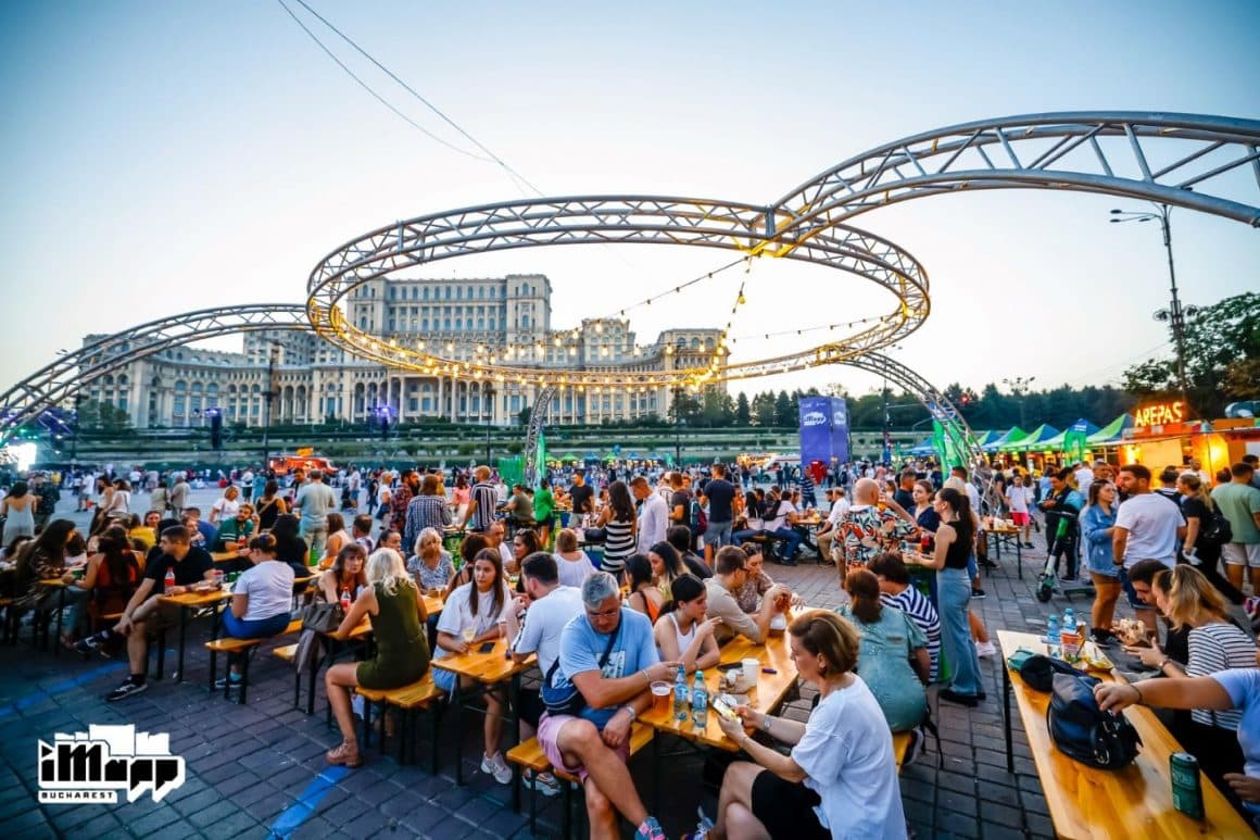 Bucharest Street Food festival, septembrie 2024. Mai multi oameni asezati la mese de lemn, la un festival de street food, in Piata Constitutiei Bucuresti