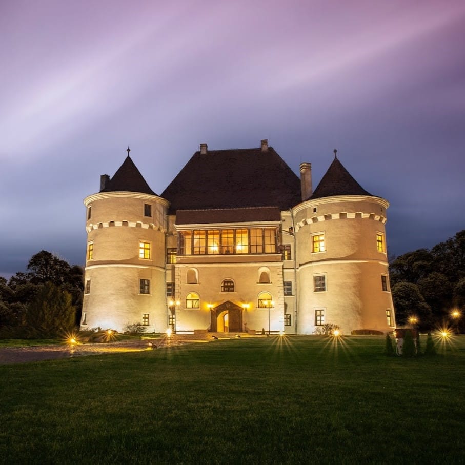 Castelul Bethlen-Haller fotografiat seara, iluminat din exterior, cu gazon in fata si cerul movuliu in spate