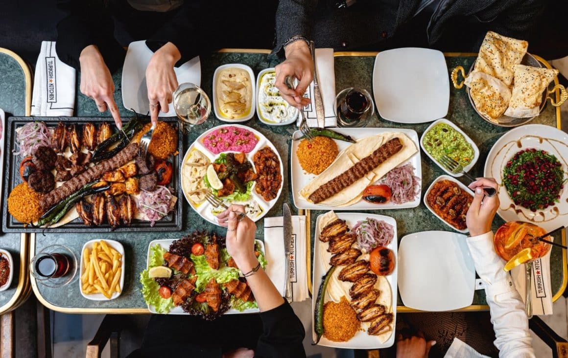 Platouri cu kebab Adana, carne la grătar, lipie, hummus, salată cu rodie și pilaf servite pe masă la Turkish Kitchen, unul dintre restaurantele turcești din București.