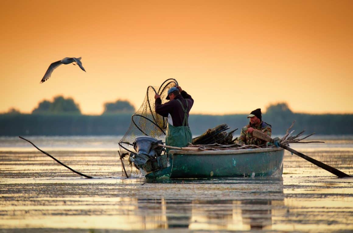 barca cu 2 pescari fotografiata la apus, pe apa, la Tulcea