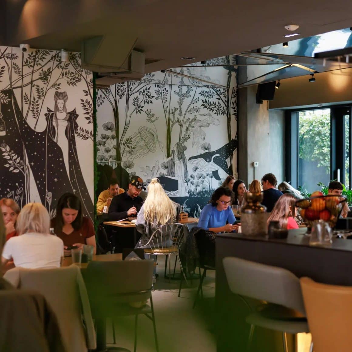 mai multi oameni iau masa in interior la restaurant Ever After Bucuresti, decorat cu un perete alb negru, cu imagini ca din povesti. Restaurante Amzei