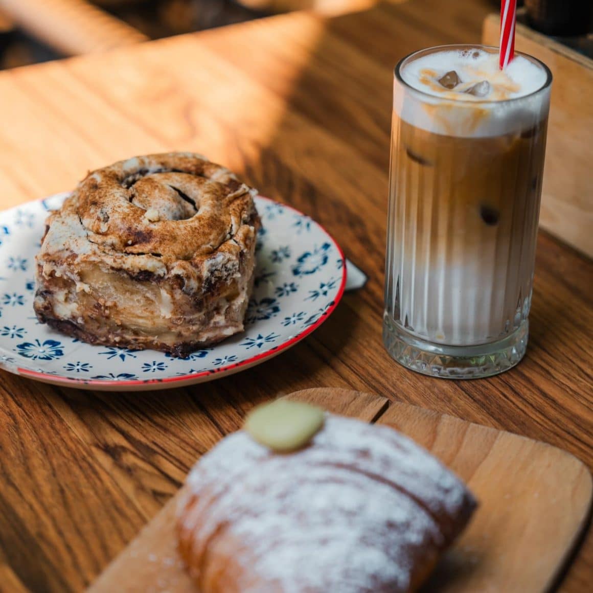 o farfurie cu cinnamon roll, un pahar cu caffee latte si un croissant