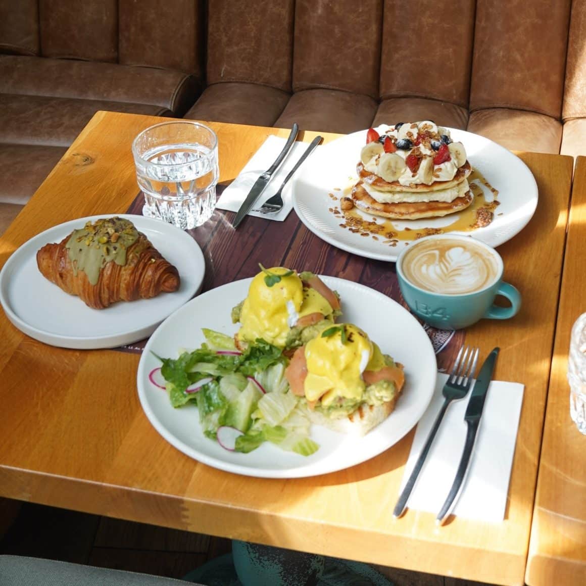 3 farfurii pe masa de lemn, cu clatite cu crema si fructe de padure, croissant si oua posate de la B4 Market unde să iei brunch în București