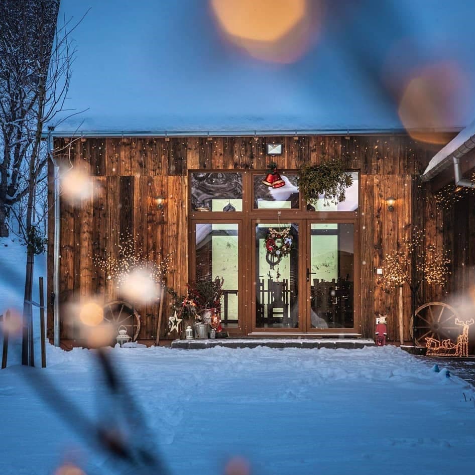 Casa Trappold, una din pensiuni cu ciubăr, fotografiată iarna, seara, cu casa si curtea pline de zapada si beculete la geam