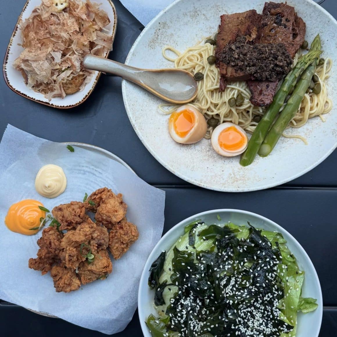 Meniu japonez cu ramen în București, servit la restaurantul Nishibo, cu noodles, ou marinat, carne fragedă, sparanghel, pui crispy și salată de alge, fotografiat de sus.