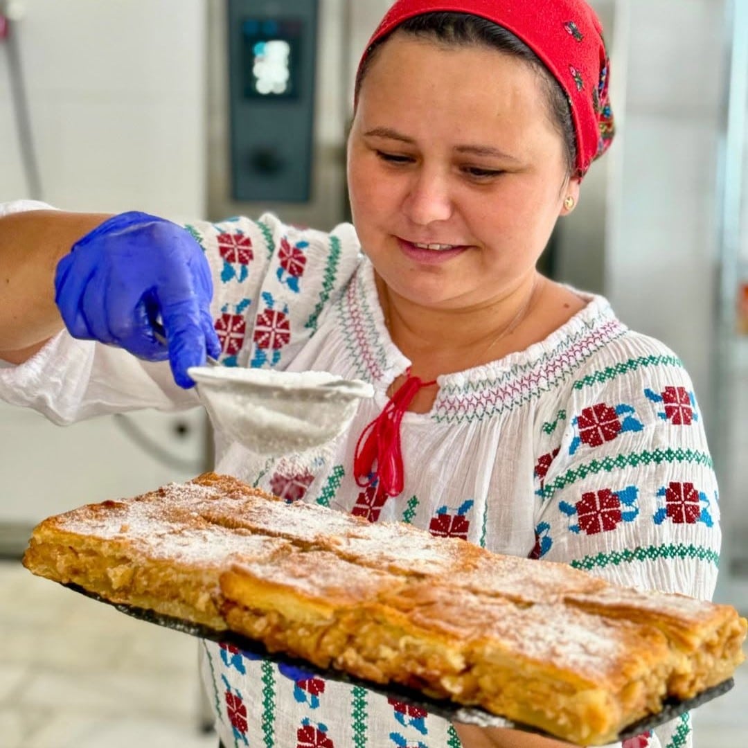 Femeie presara zahar pudra peste o placinta traditional romaneasca la Scovergaria Micai
