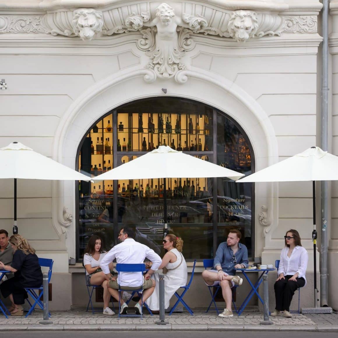 Oameni la mese asezate pe trotuar in fata brasseriei La Mita Biciclista
