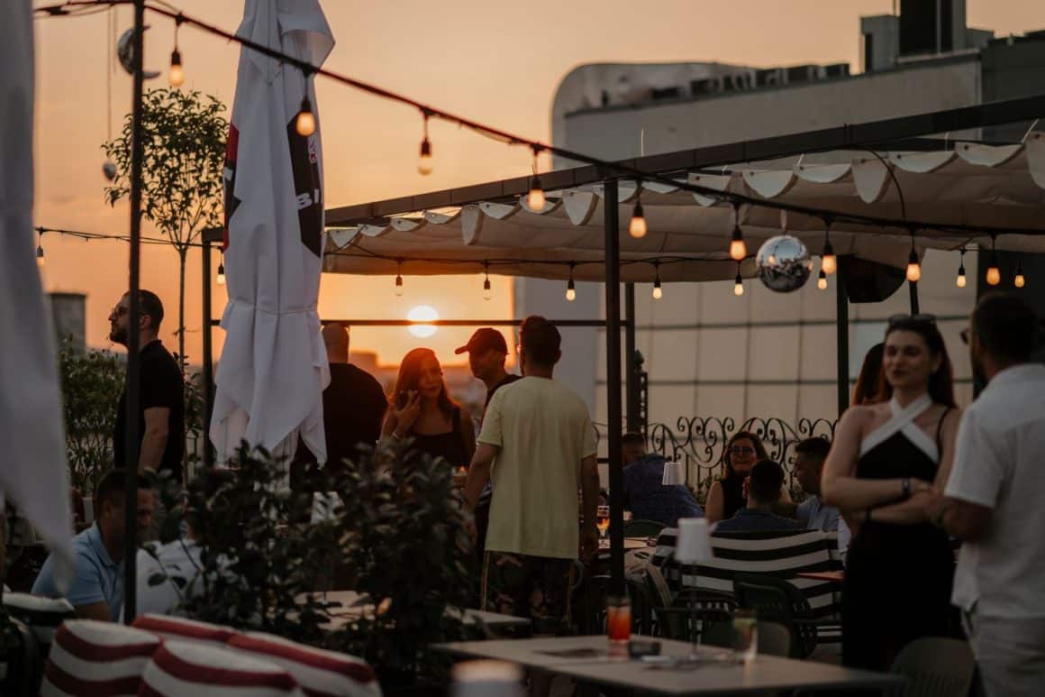 Mai mulți oameni pe terasa Bartini Rooftop Bar & Restaurant, vara la apus, socializeaza