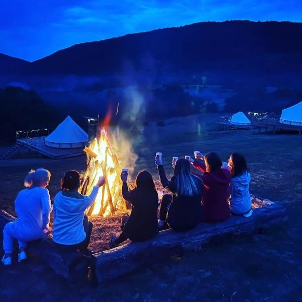 mai mulți oameni strânși in jurul unui foc de tabara la The Hunters Glamping. Cele mai frumoase campinguri din România