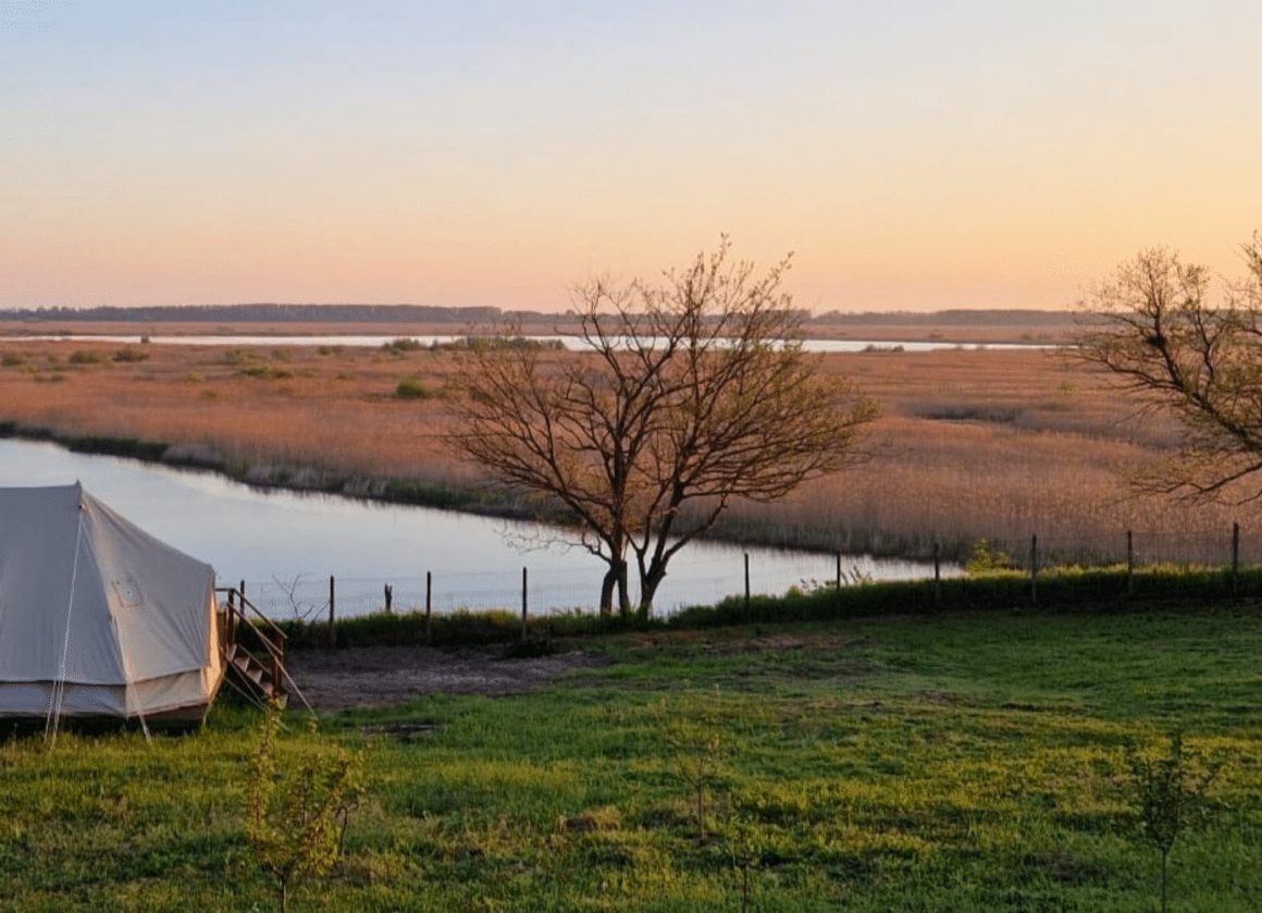 cort asezat pe iarba, iar in fundal se vede Dunărea. Cele mai frumoase campinguri din România. Delta Sunrise
