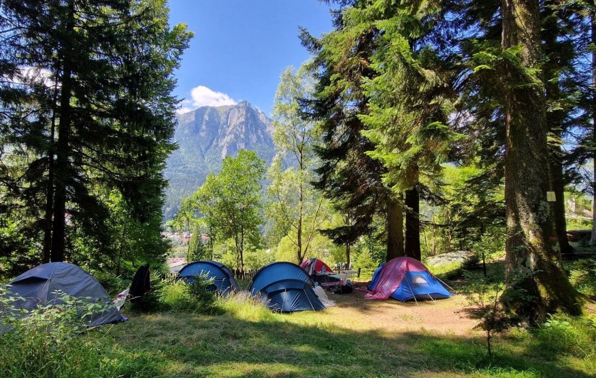 mai multe corturi asezate intr-o poienita intre brazi, iar in fundal munții Bucegi. Hay Huy Camp. Cele mai frumoase campinguri din România. 