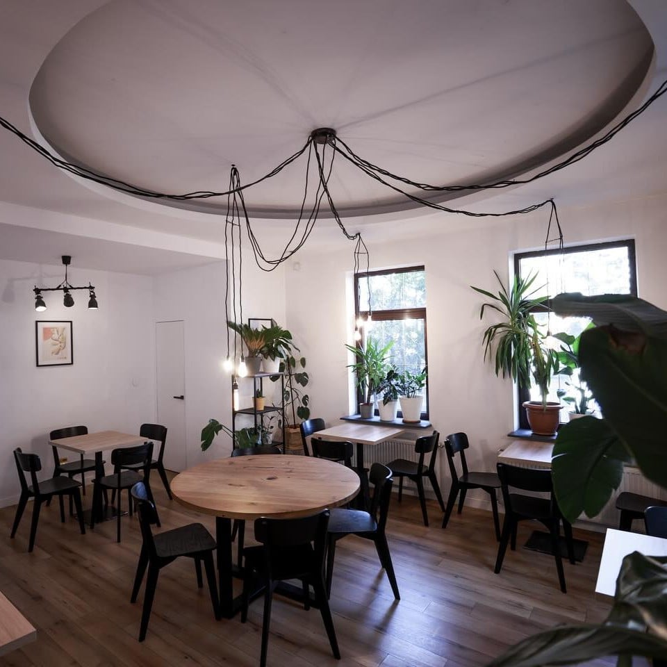 Replace are un interior minimalist, cu mese rotunde din lemn și scaune simple, oferind un spațiu liniștit pentru lucru sau întâlniri.