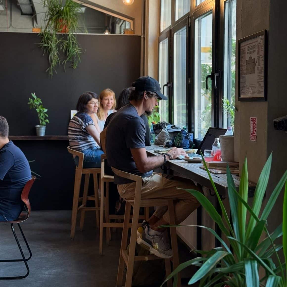 Interior luminos și aerisit la Beans & Dots, unde mesele de lemn și plantele verzi creează un spațiu relaxat, ideal pentru a lucra concentrat la laptop.