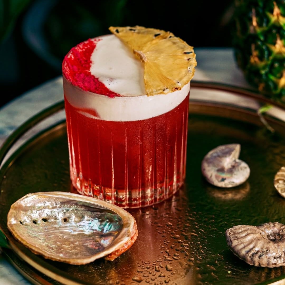 O variantă fresh și colorată, cu spumă și felie de ananas, arată cum un cocktail legendar poate fi reinterpretat cu un twist tropical. Negroni Week în București. Caribbean Sour