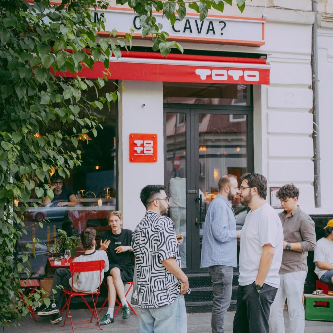 Mai multi oameni stau de vorba afara, vara, in fata la Bar Toto Bucharest, loc cu tapas și vermut în București