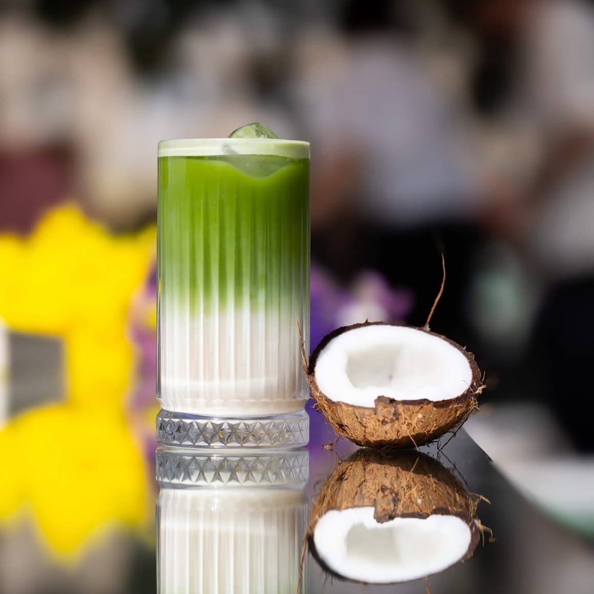 Matcha în București la Boiler – iced matcha latte stratificat, servit în pahar înalt, cu lapte și gheață, decorat cu jumătate de nucă de cocos.